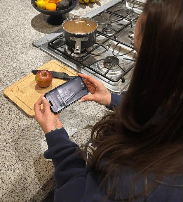A woman holding a smartphone displays the Babysense FullPeek Smart WiFi Baby Monitor live feed of a crib, demonstrating the baby wireless HD camera's view