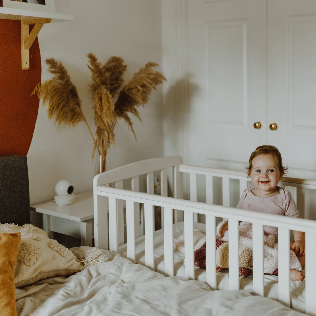 A smiling baby in a white crib while a white Babysense HD S2 video baby monitor with a non wifi camera sits on a nearby nightstand