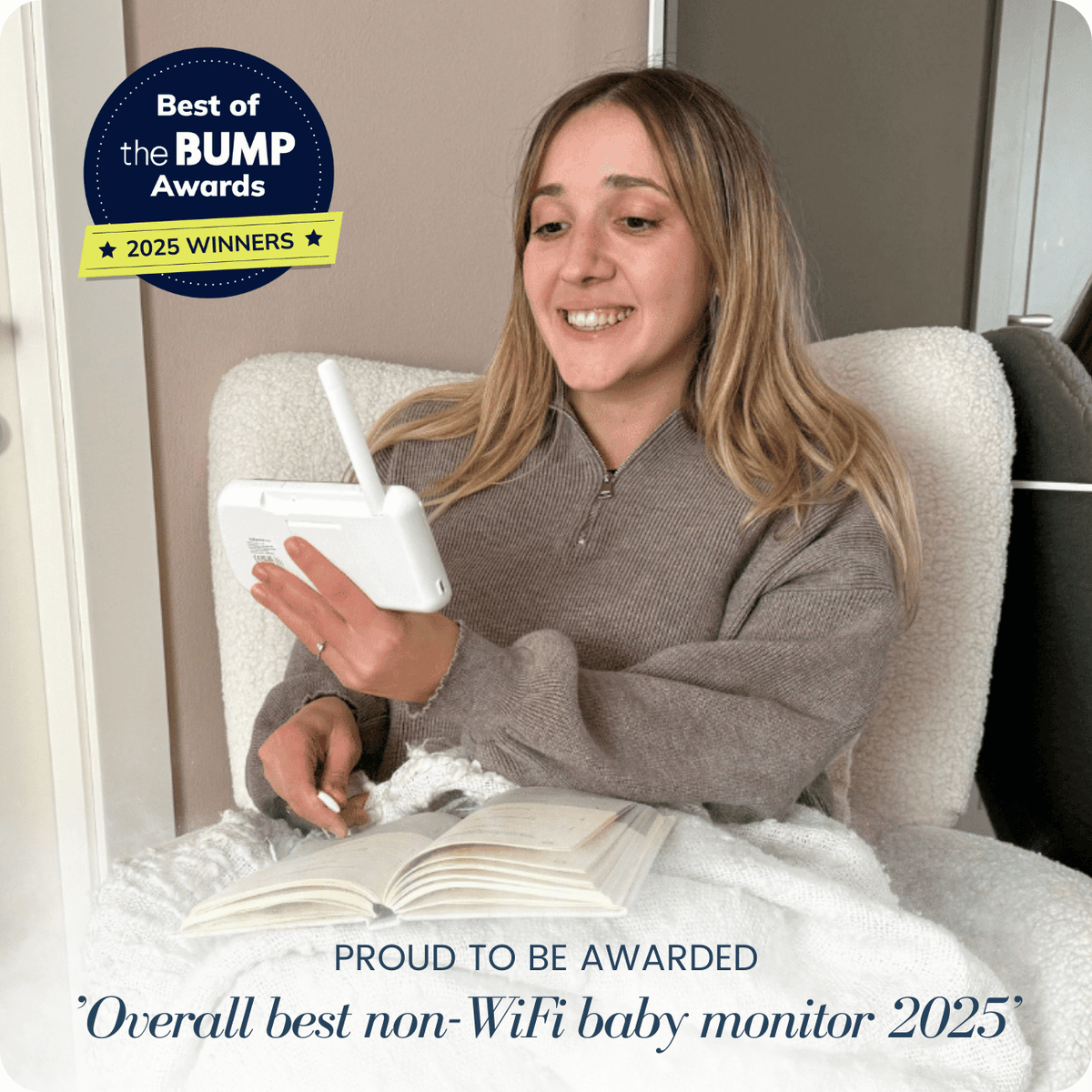 A smiling woman sits comfortably, holding a white Babysense PRO non-WiFi video baby monitor with 2 cameras, showcasing its use
