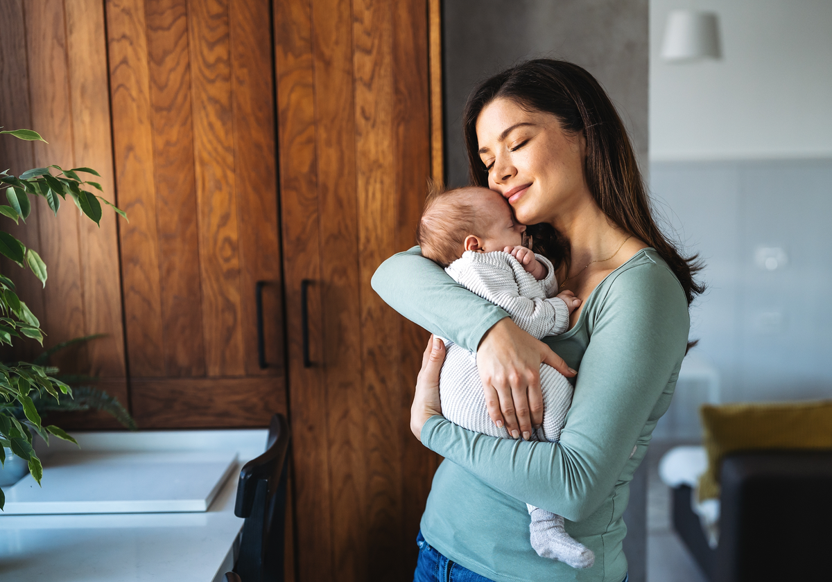 A loving mother wearing a green long-sleeved shirt is seen gently holding her infant, underscoring the need for essential HSA/FSA eligible products like a baby monitor with both wifi and non wifi options to ensure a baby's safety and well-being