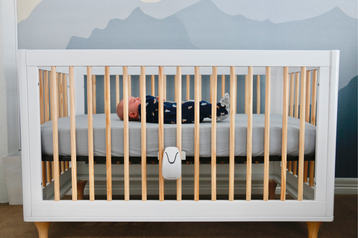 Baby lying in a crib with a mountain mural on the wall