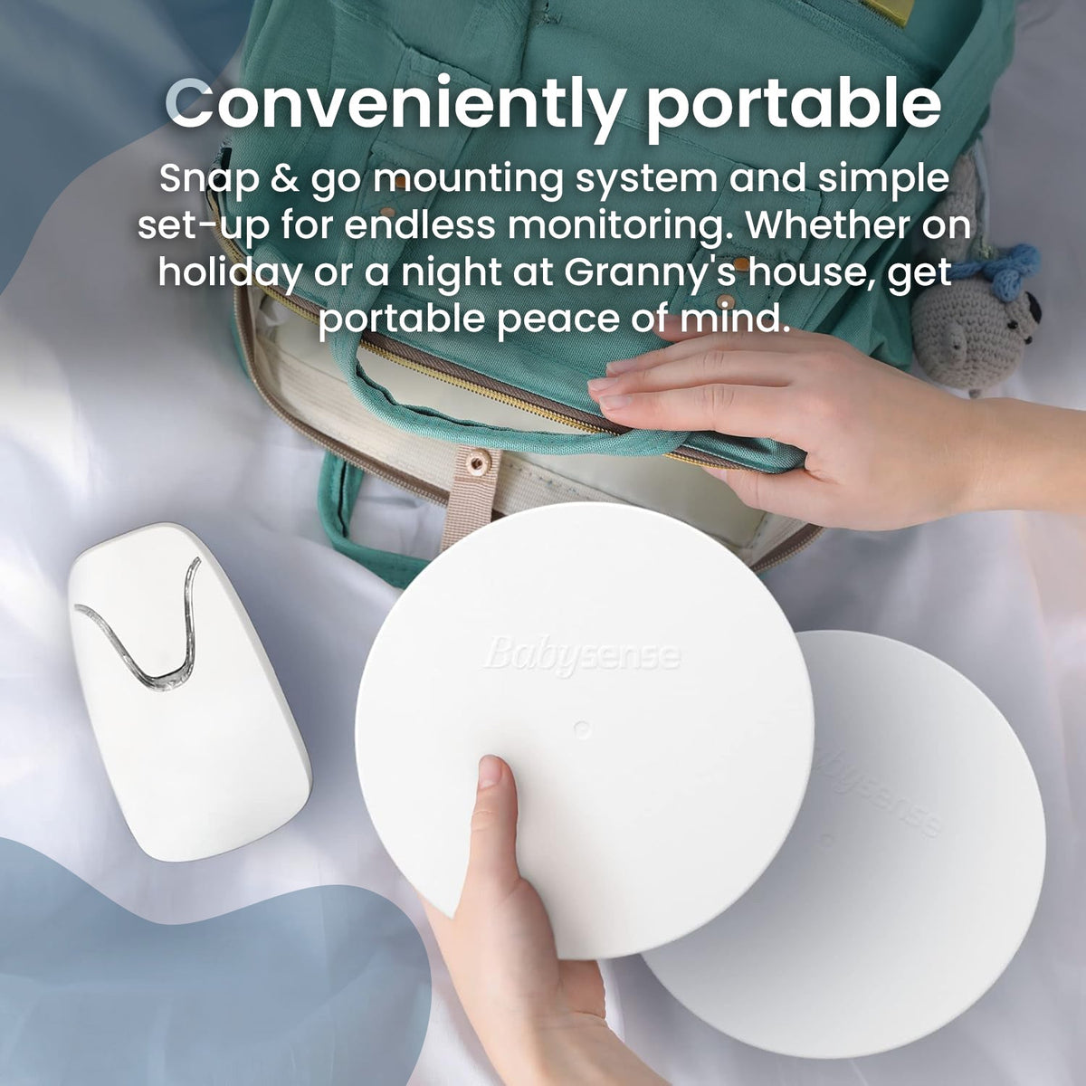 A person is holding two white, circular Babysense 7 sensors and a white monitoring unit with a silver accent, ready for convenient and portable baby monitoring