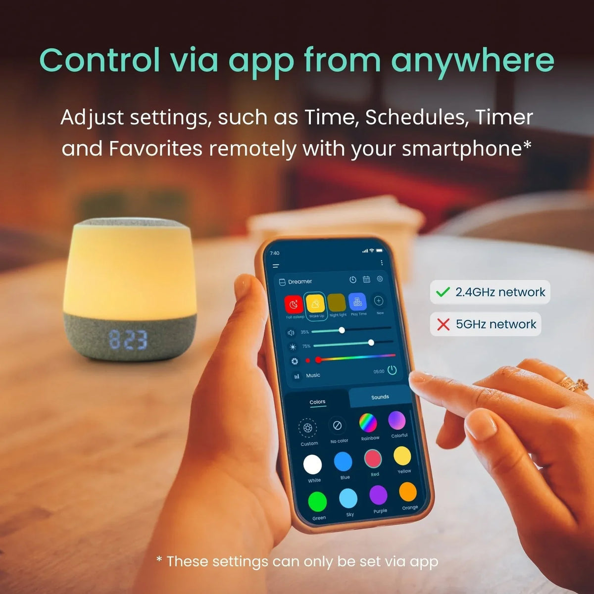 A hand holds a smartphone displaying the Babysense Dreamer 2.0 & Pro app, showing controls for colors and sounds, with the smart nursery light and LED clock 8:23 glowing softly on a wooden surface