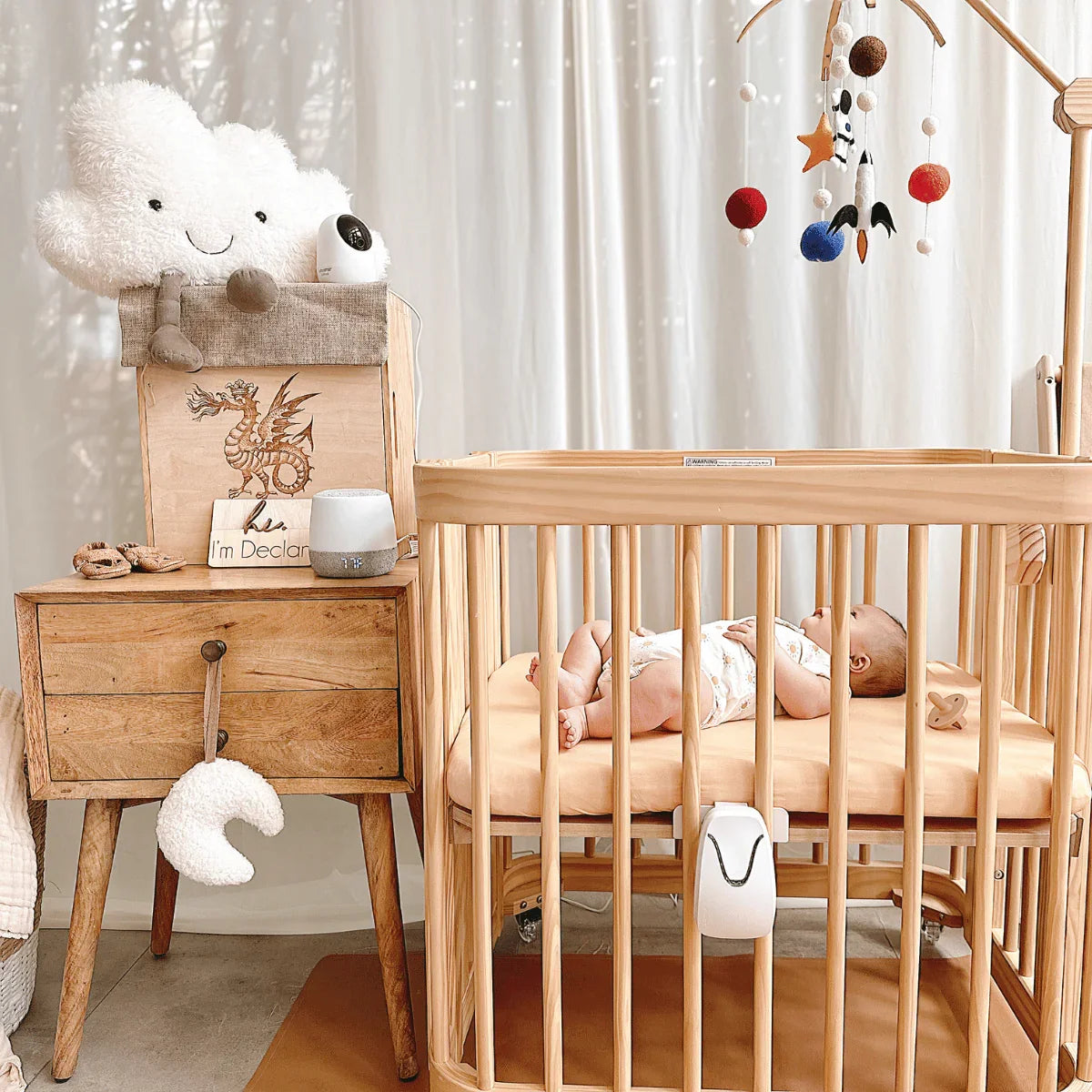 This nursery features the Babysense Total Sleep & Monitoring Solution with a close-up of the hd video baby monitor mounted on a light wood crib with a baby sleeping soundly